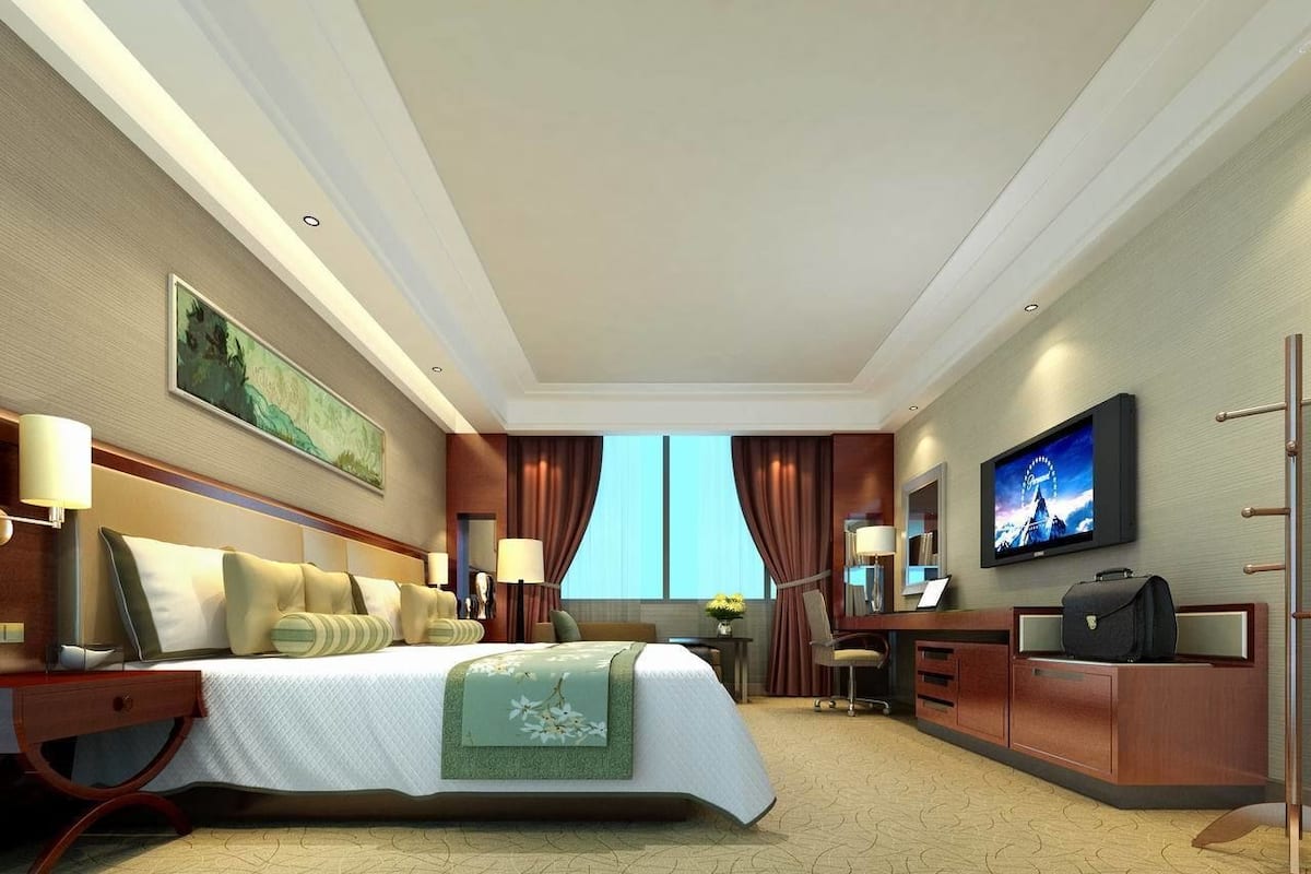 Een hotelkamer met een groot bed, een bureau met stoel, een televisie en een raam met gordijnen.