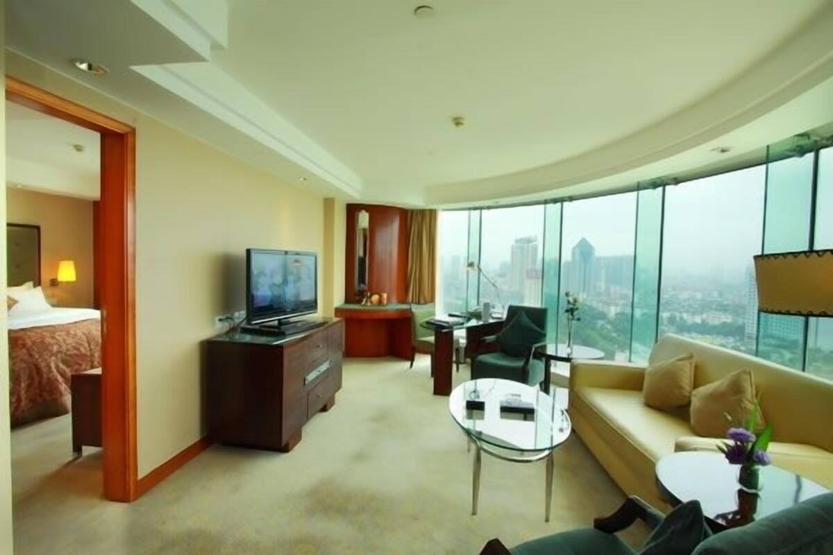Een moderne hotelkamer met een groot bed, een televisie, een bureau, een sofa en uitzicht op de stad.