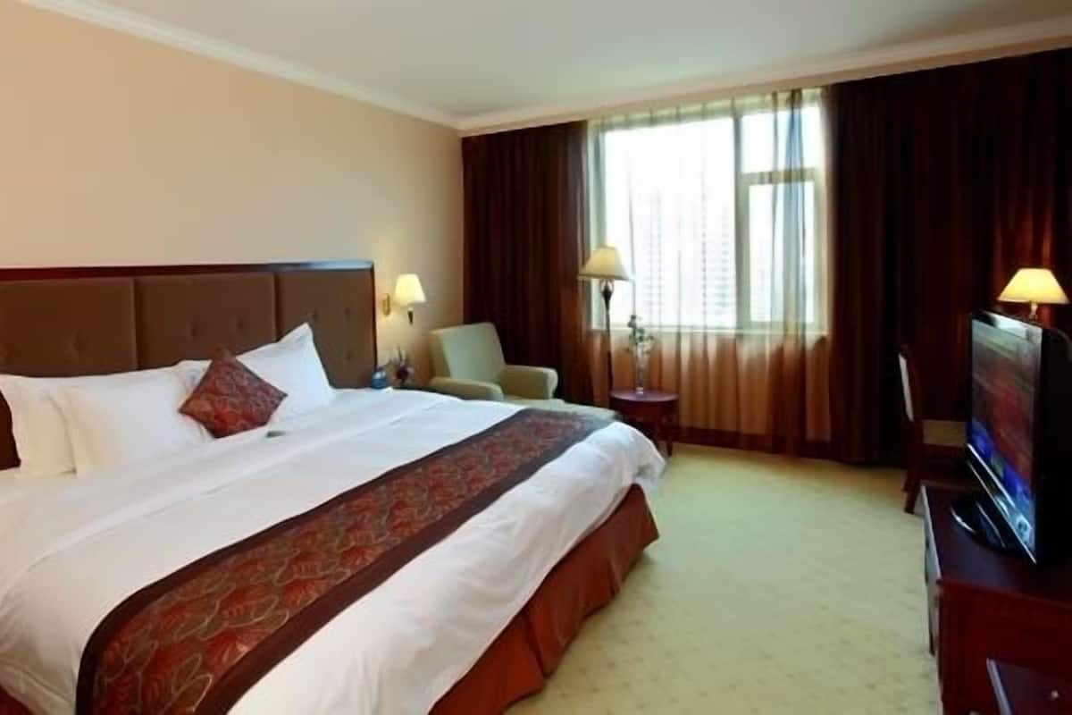 Een hotelkamer met een groot bed, twee bedlampen, een stoel, een televisie en een raam met gordijnen.