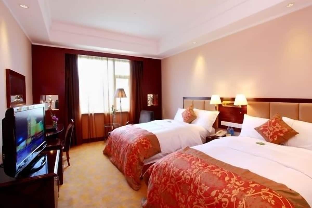 Een hotelkamer met twee bedden, een televisie, een bureau en een raam met gordijnen.