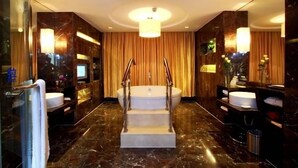 A luxurious bathroom with a marble floor, a central bathtub, and two sinks.