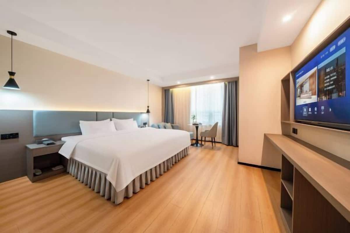 Une chambre d’hôtel moderne équipée d’un grand lit, d’un bureau, d’une chaise, d’une télévision et d’une fenêtre avec des rideaux.