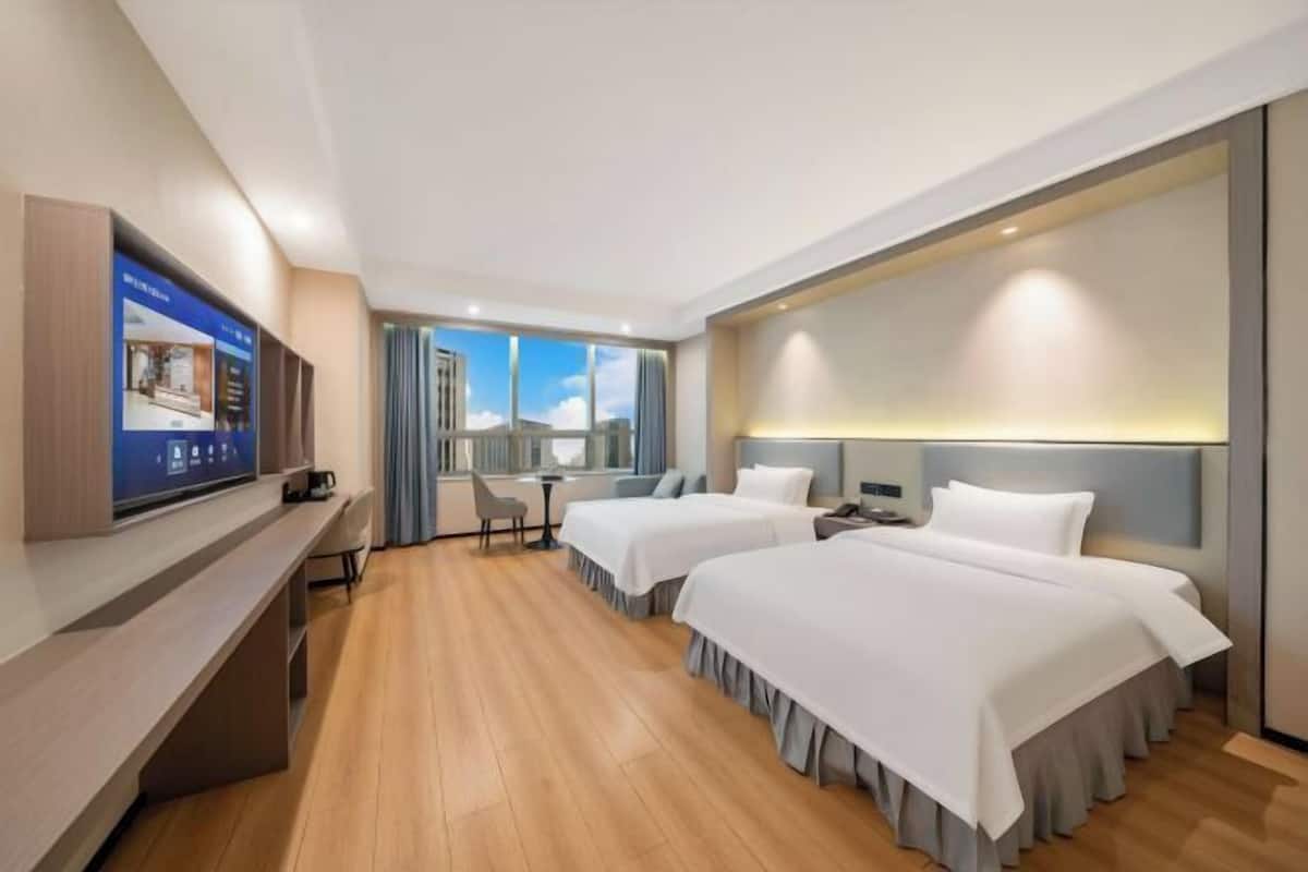 Une chambre d’hôtel avec deux lits, un bureau avec un ordinateur, une télévision et une vue sur l’extérieur.