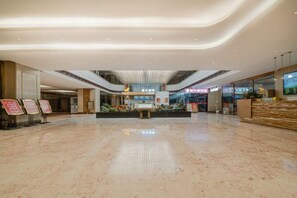 Un hall d’entrée spacieux et moderne, doté d’un sol en marbre poli, d’un comptoir de réception central et d’un plafond haut avec un éclairage intégré.