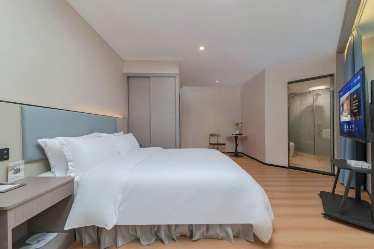 Une chambre d ’hôtel moderne équipée d’un lit, d’un bureau, d’une petite table, d’un tapis de course et d’une porte vitrée donnant sur une salle de bain.