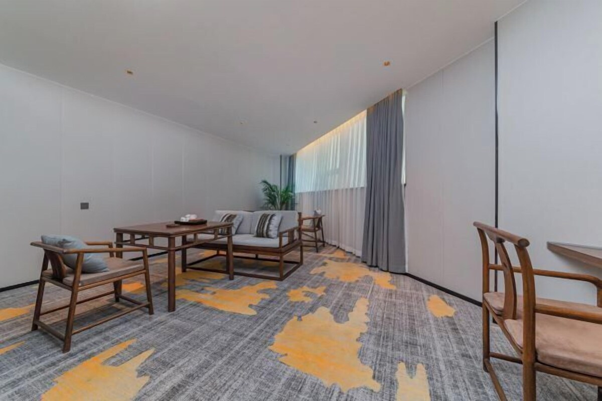 Une chambre d’hôtel avec un canapé, deux fauteuils, une petite table et une grande fenêtre avec des rideaux.