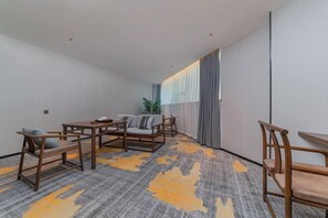 Une chambre d’hôtel avec un canapé, deux fauteuils, une petite table et une grande fenêtre avec des rideaux.