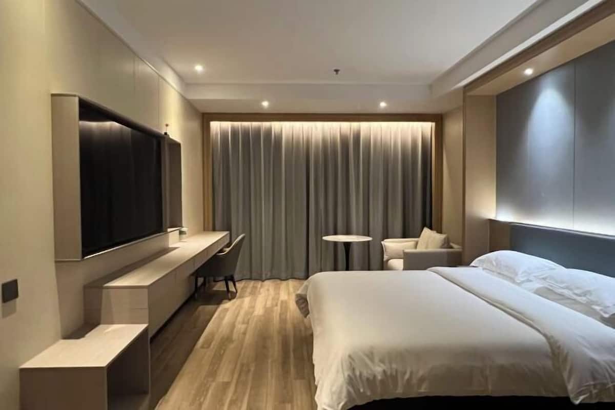 Une chambre d’hôtel moderne avec un grand lit, un téléviseur à écran plat fixé au mur, un bureau avec une chaise, une petite table ronde et un canapé.