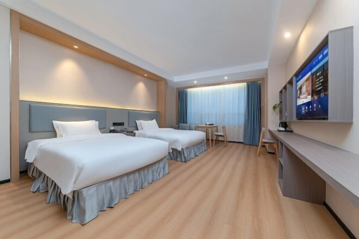 Une chambre d’hôtel avec deux lits, un bureau, une chaise et un téléviseur fixé au mur.