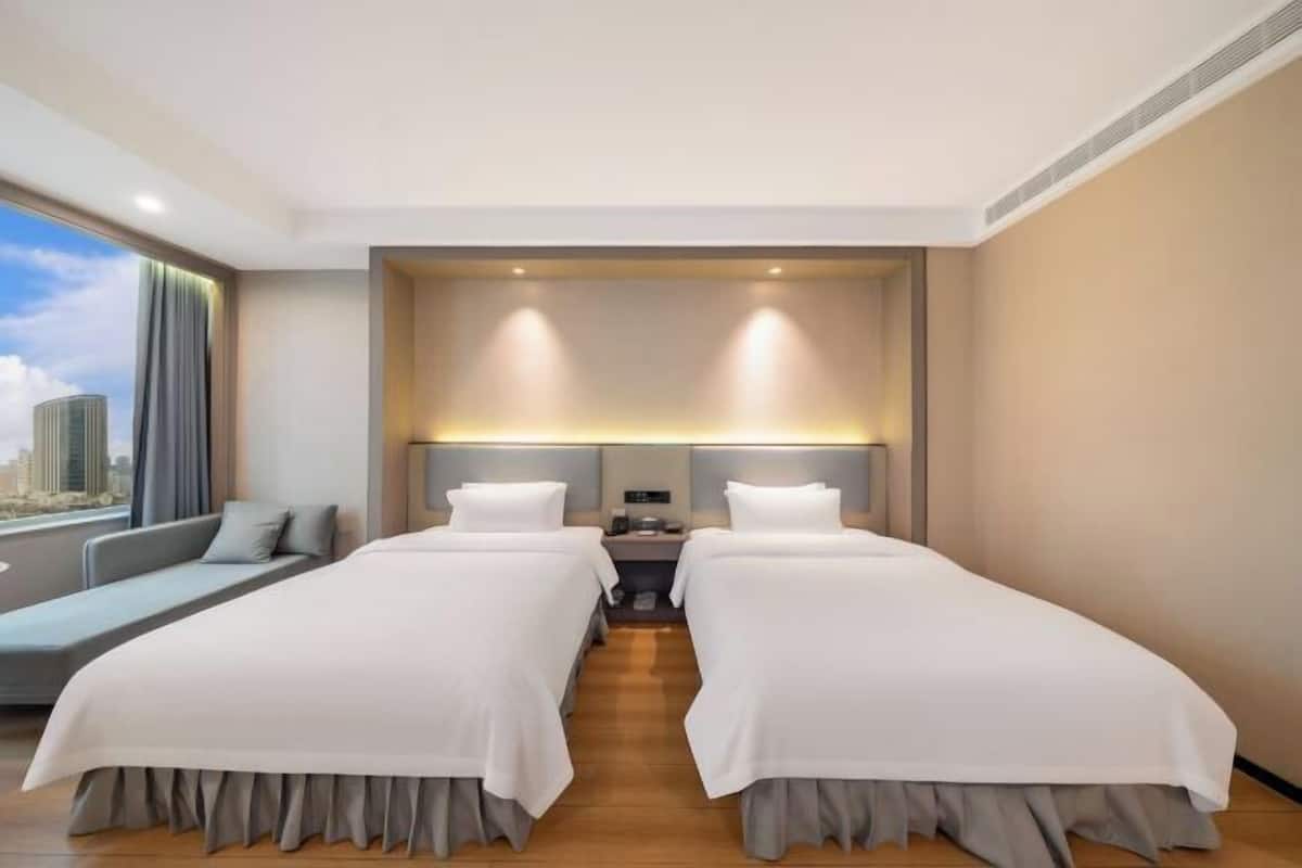 Une chambre d’hôtel avec deux lits, un canapé, une table de chevet et une vue sur la ville.