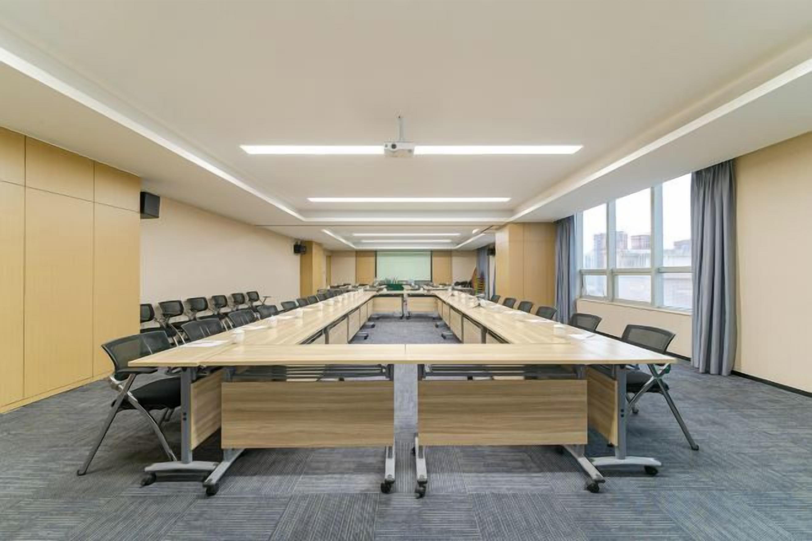 Un salón de conferencias con una larga mesa, sillas, piso alfombrado y grandes ventanales.