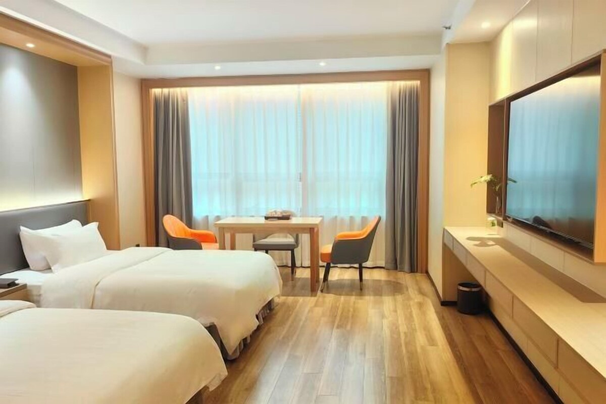 Une chambre d’hôtel avec deux lits, une table à manger avec des chaises, une télévision et une grande fenêtre avec des rideaux.