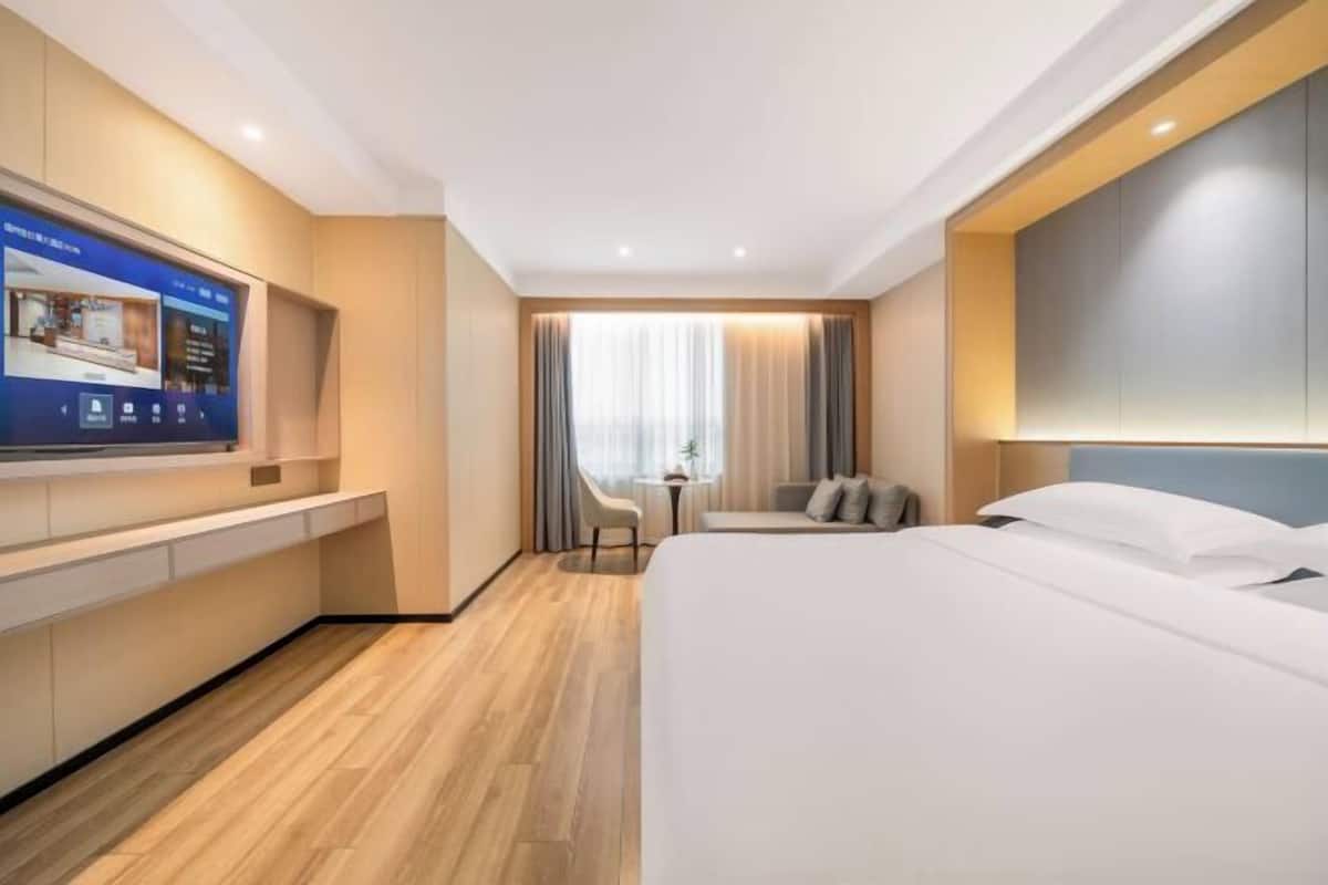 Une chambre d’hôtel moderne dotée d’un grand lit, d’un téléviseur fixé au mur, d’une petite table et d’un coin salon avec un fauteuil.