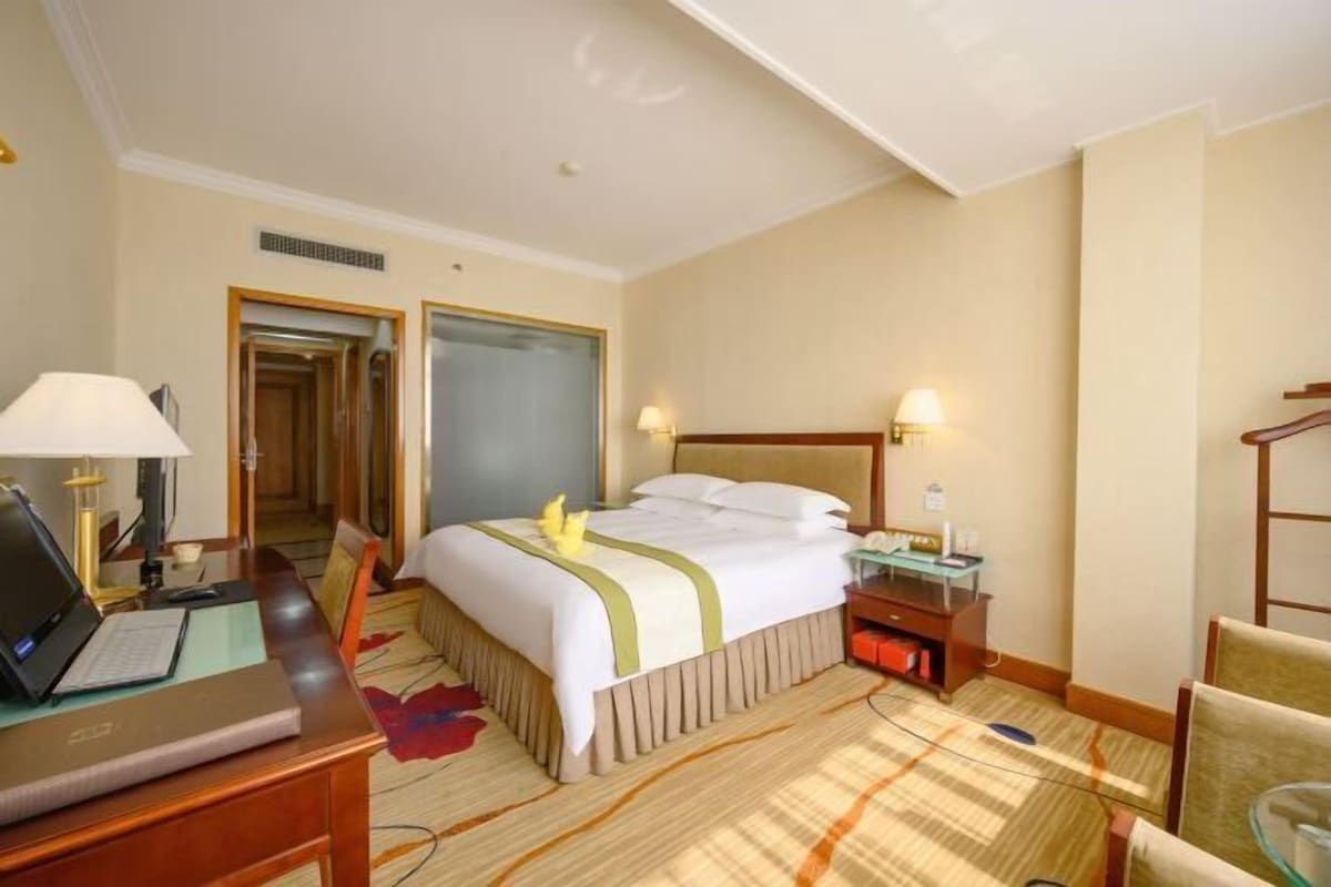 A hotel room with a bed, desk, chair, and a mirror.