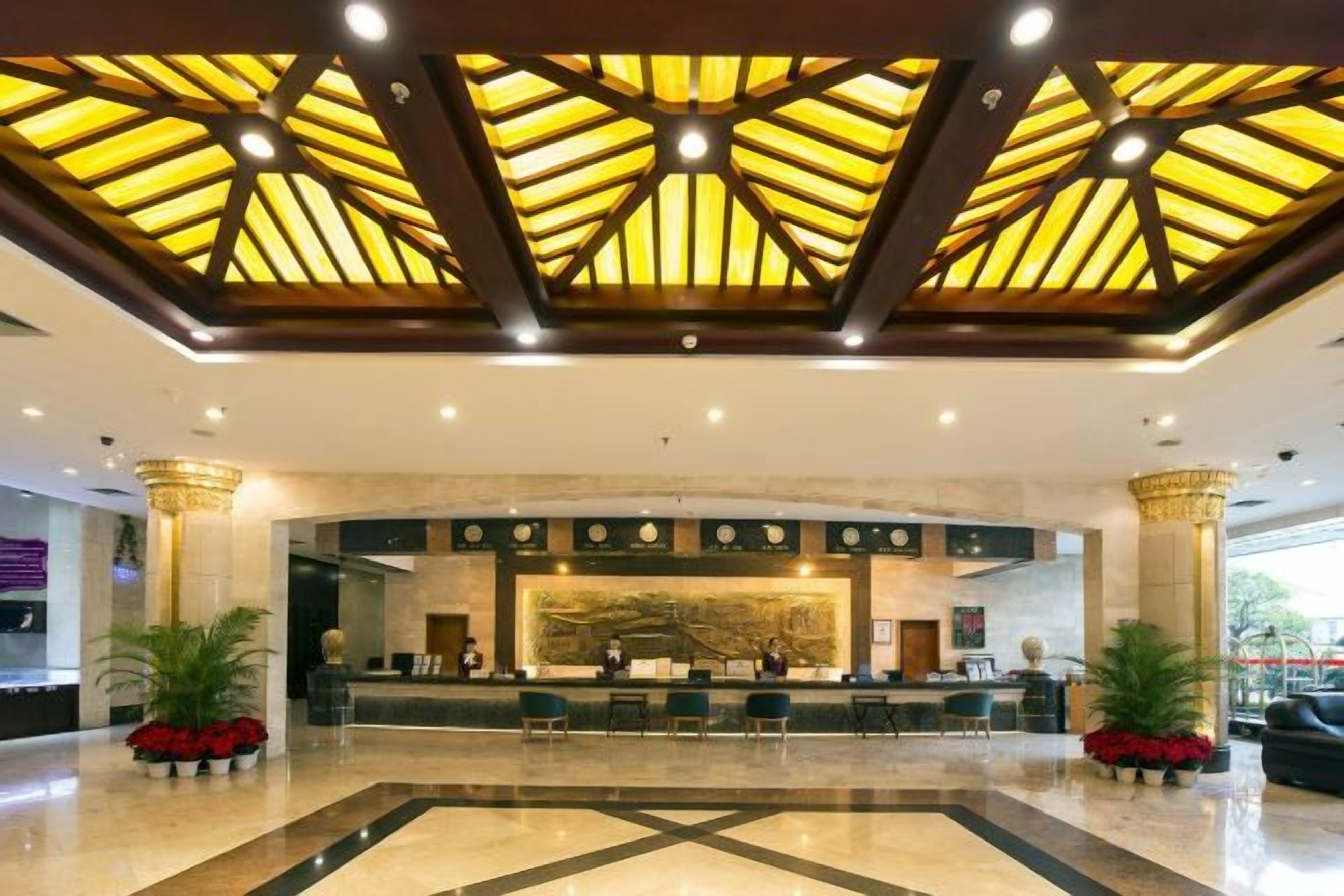 A hotel lobby with a reception desk, seating area, and a geometric ceiling design.
