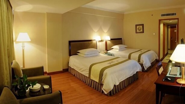 Quarto de hotel com duas camas, uma escrivaninha, uma cadeira, um abajur e uma pequena mesa com uma planta.
