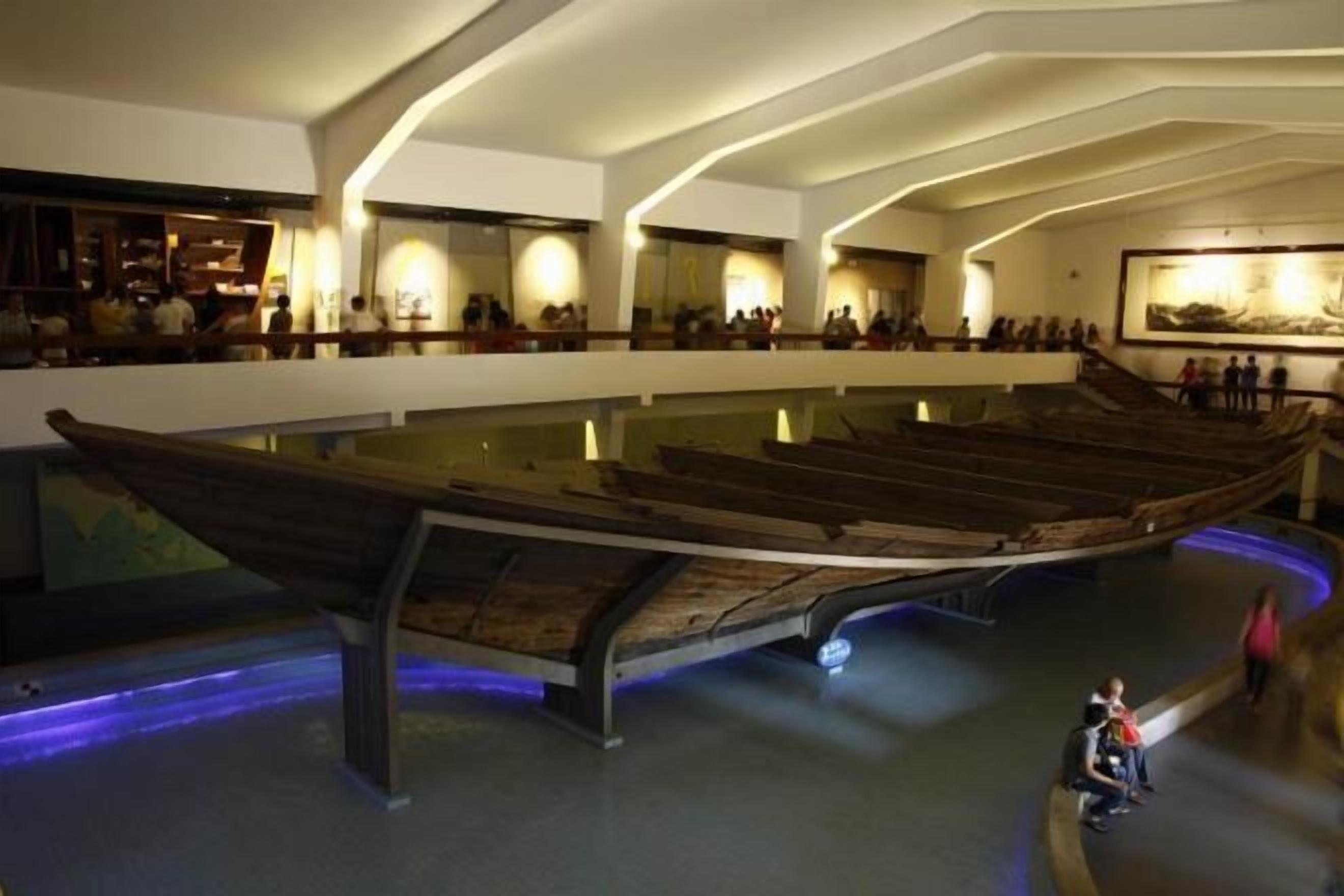 A museum with a large wooden boat exhibit in the center, surrounded by visitors.