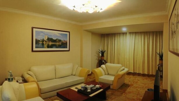 A living room with a sofa, two armchairs, a coffee table, a television, and a framed picture on the wall. - Overseas Chinese Hotel (Quanzhou)