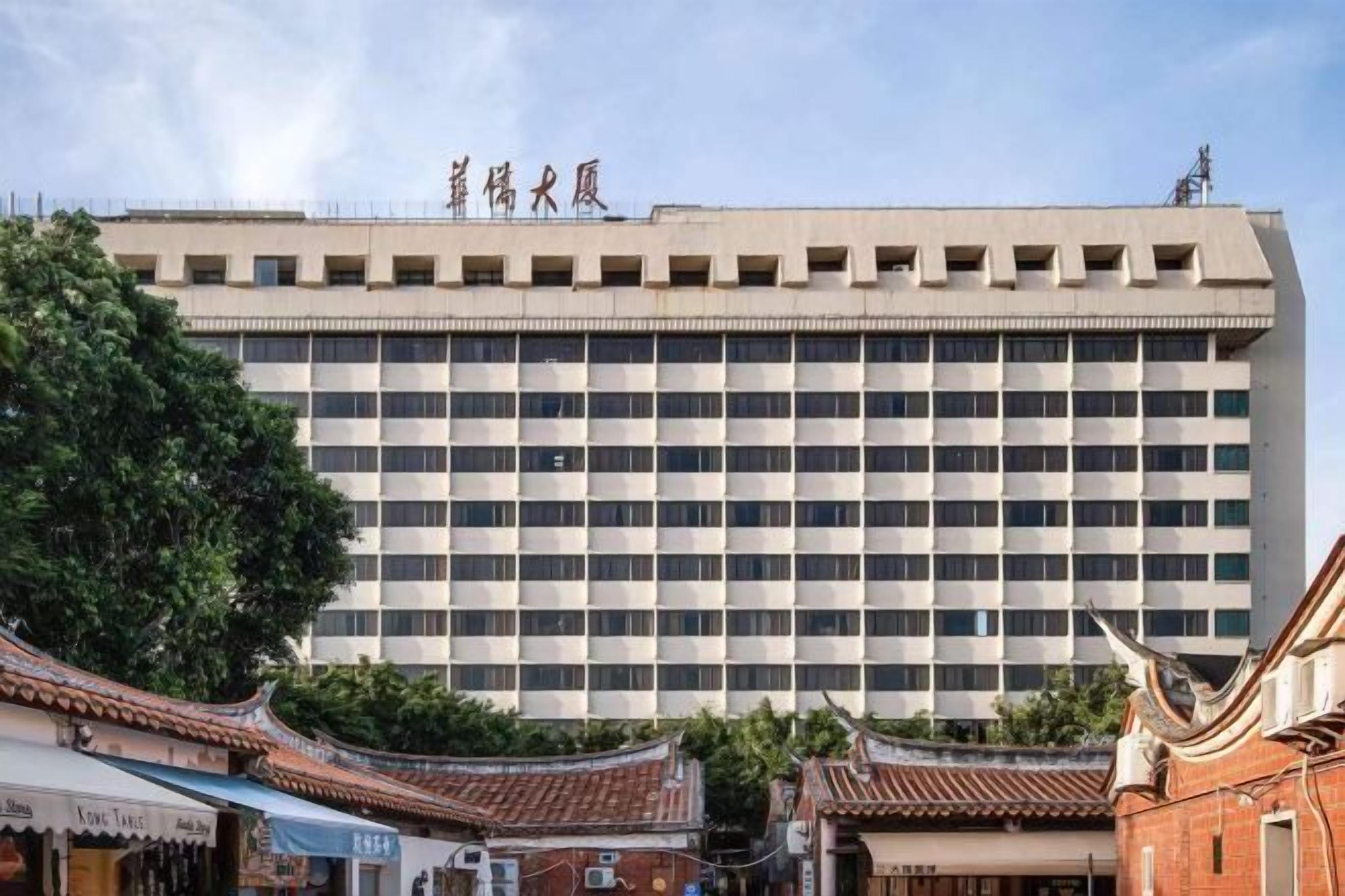 A multi-story building with a grid of windows, traditional-style roofs in the foreground, and a sign with Chinese characters at the top.
