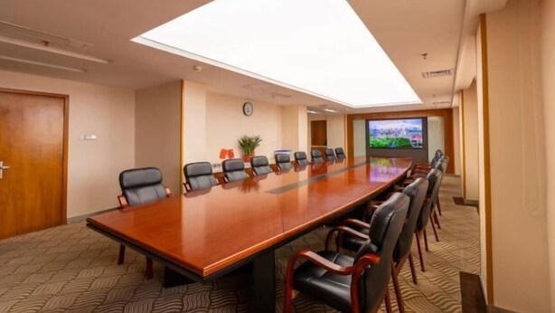 A conference room with a long table, chairs, a clock, a plant, and a TV screen. - Overseas Chinese Hotel (Quanzhou)