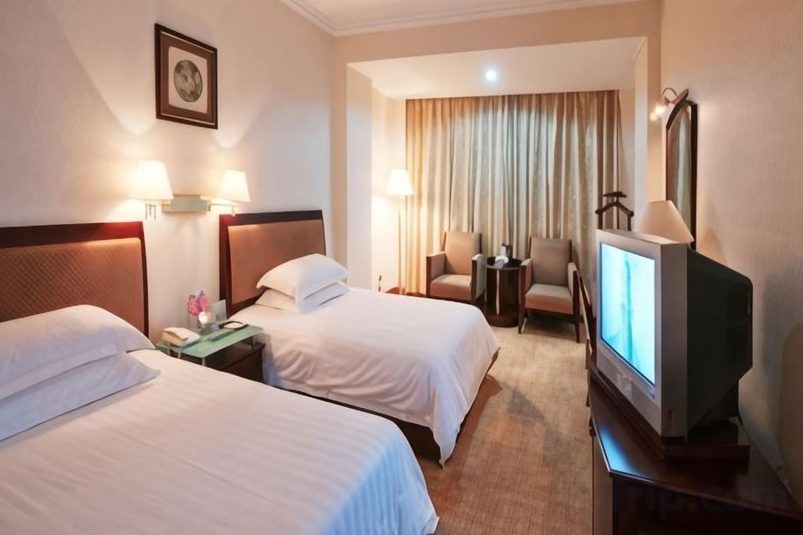 A hotel room with two beds, a television, a desk with a lamp, and a chair.