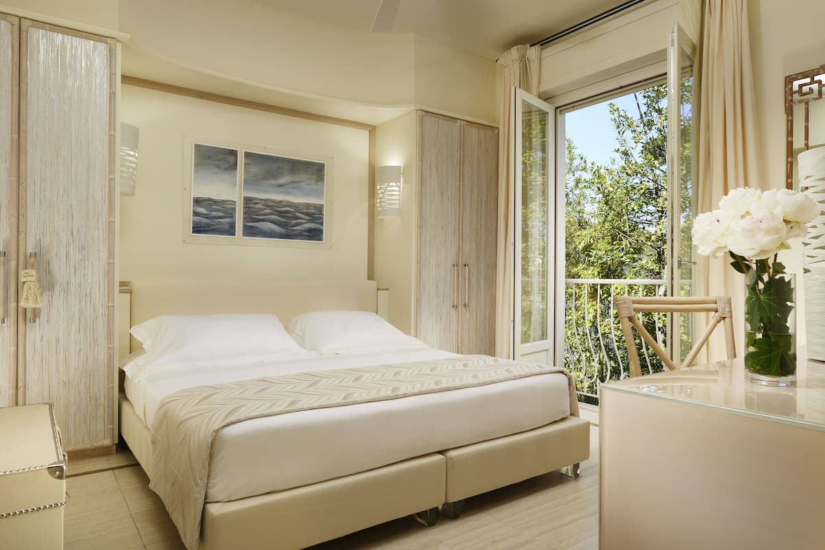 A bedroom with a bed, a dresser, a window with a view of greenery, and a painting on the wall.
