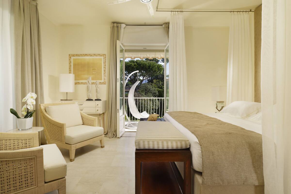 A bedroom with a bed, a chair, a bedside table, and a view of the outdoors.