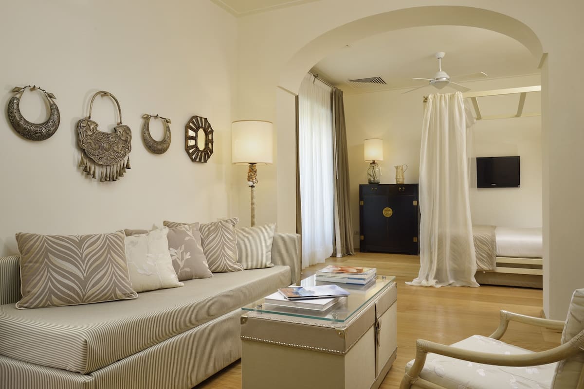 A modern hotel room with a sofa, a glass coffee table, a chair, a bed, a TV, and a wardrobe.