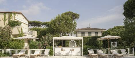 A swimming pool with lounge chairs and umbrellas, surrounded by greenery and buildings.