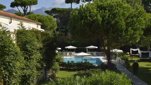 A pool area with umbrellas, surrounded by lush greenery and trees. - Villa Roma Imperiale (Forte dei Marmi)