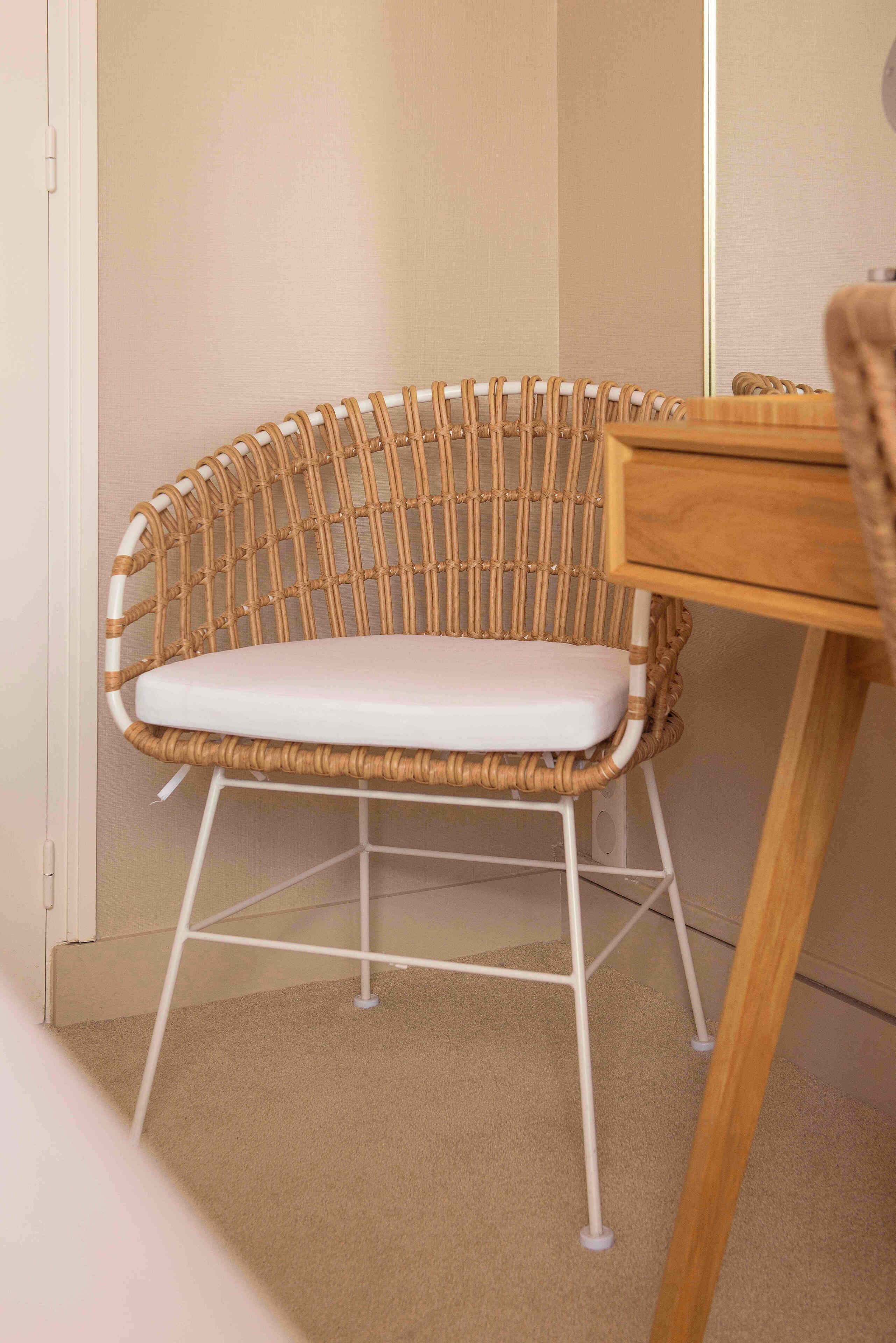 A wicker chair with a white cushion, a wooden side table, and a white metal frame.
