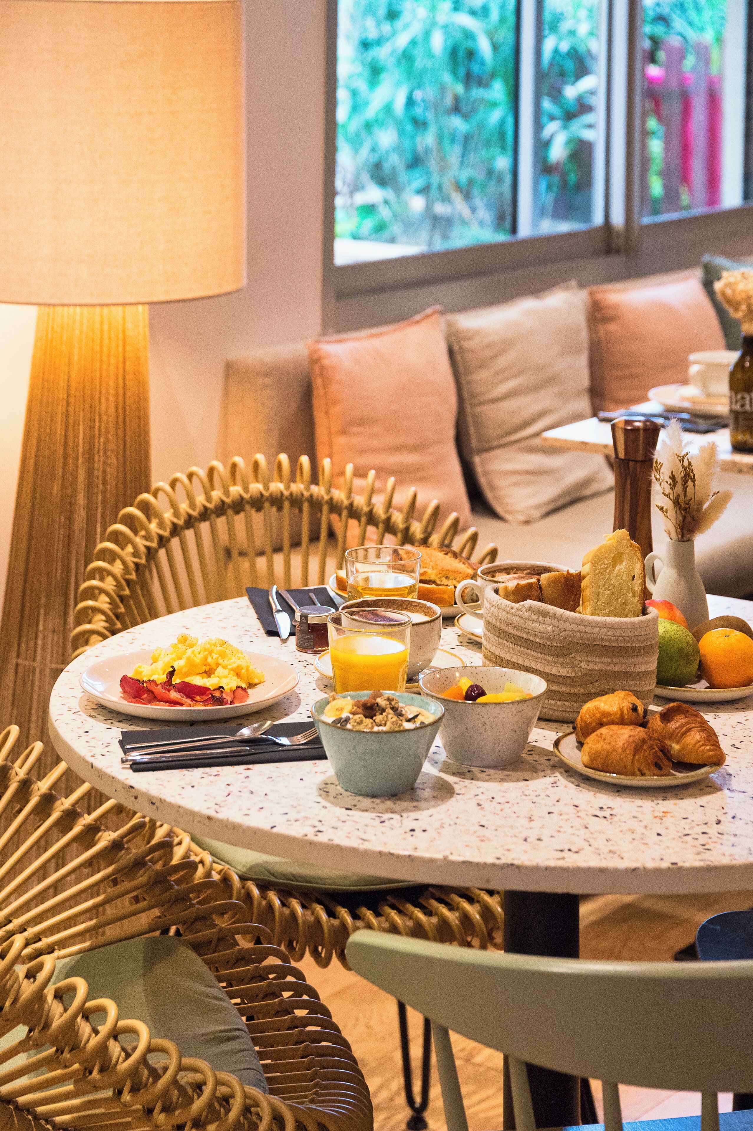 A breakfast setting with a wicker chair, a round table, and a window view.