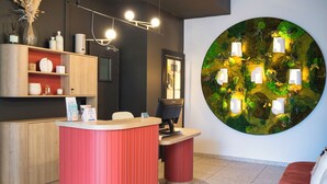 Un espace d’accueil avec un comptoir rouge, des étagères en bois et une grande décoration murale circulaire.