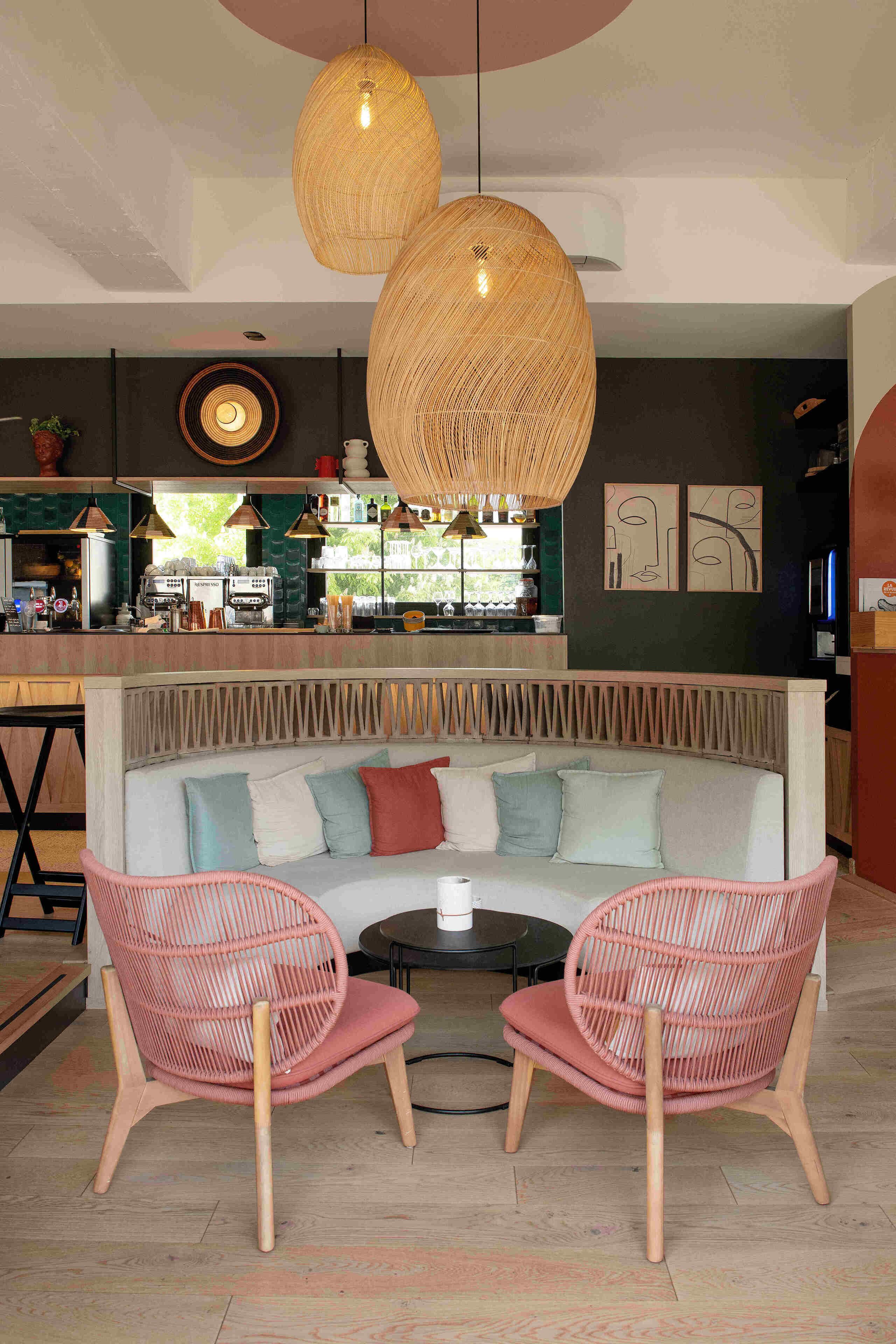 A cozy seating area with a sofa and two chairs, a bar in the background, and hanging wicker lamps.