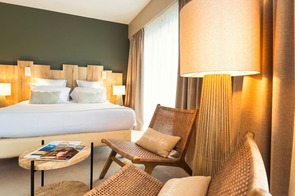 Ein Hotelzimmer mit einem großen Bett, zwei Nachttischen, einem Sessel, einem Sofa und einer Lampe.