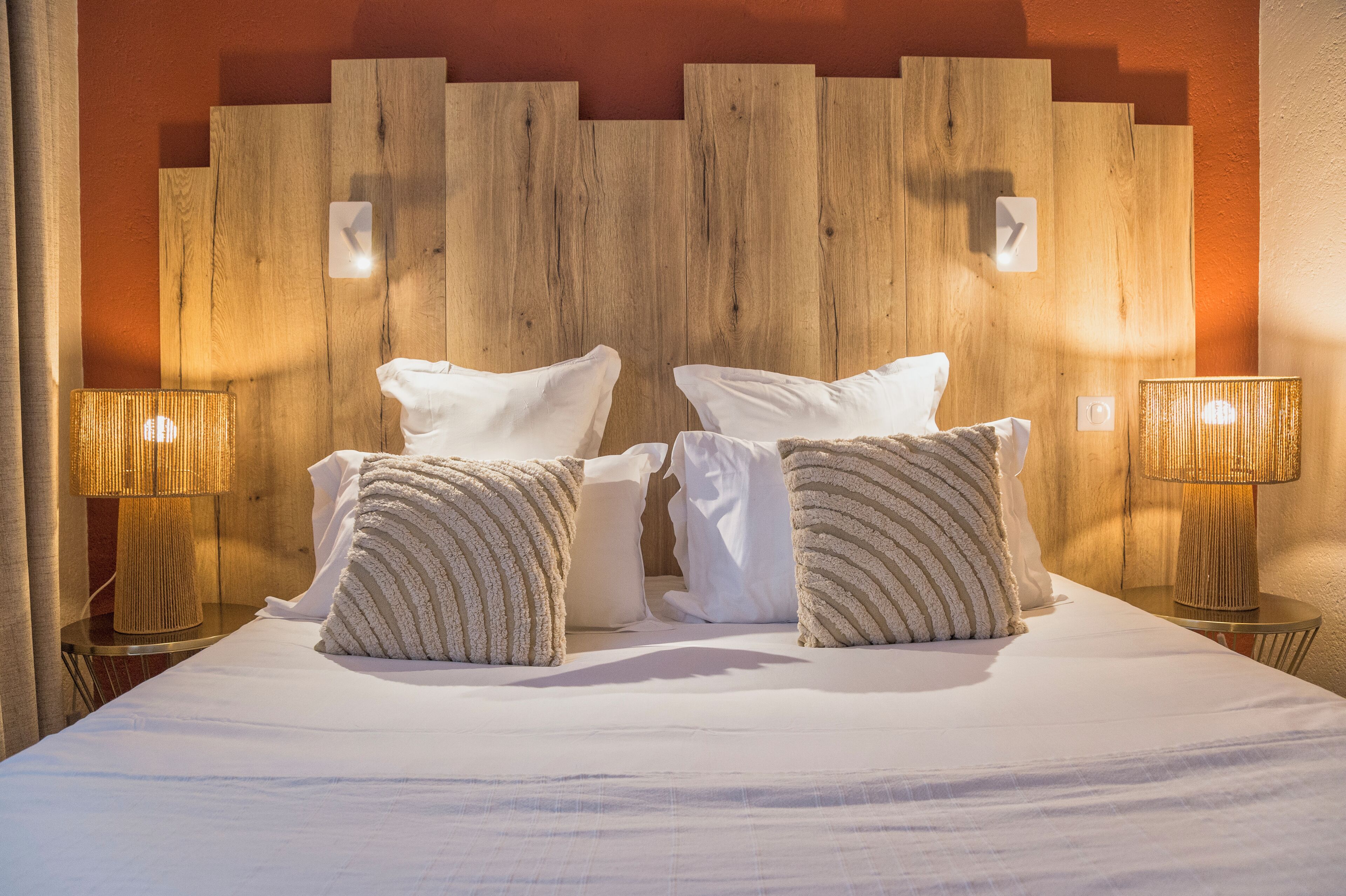 A neatly made bed with white linens and striped pillows, flanked by two bedside lamps on wooden nightstands.