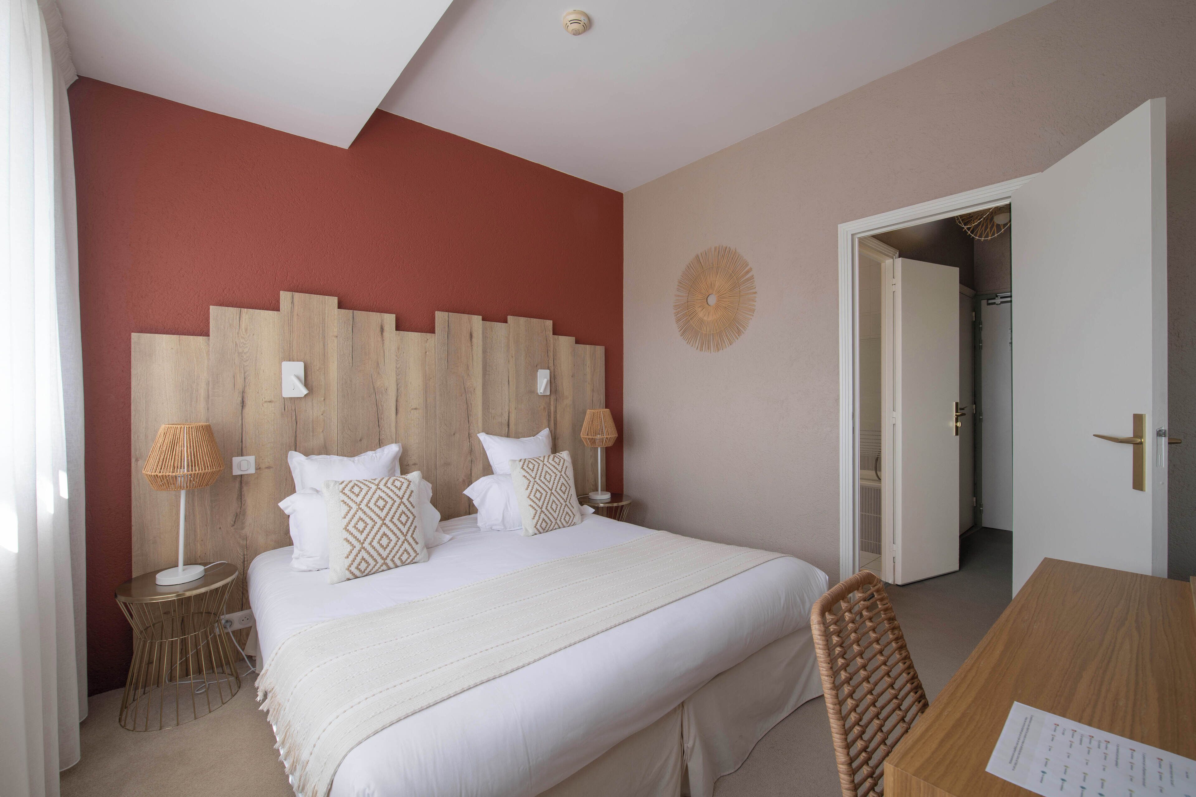 Een slaapkamer met een groot bed, een houten hoofdbord, twee nachtkastjes met lampen en een deur naar een badkamer.