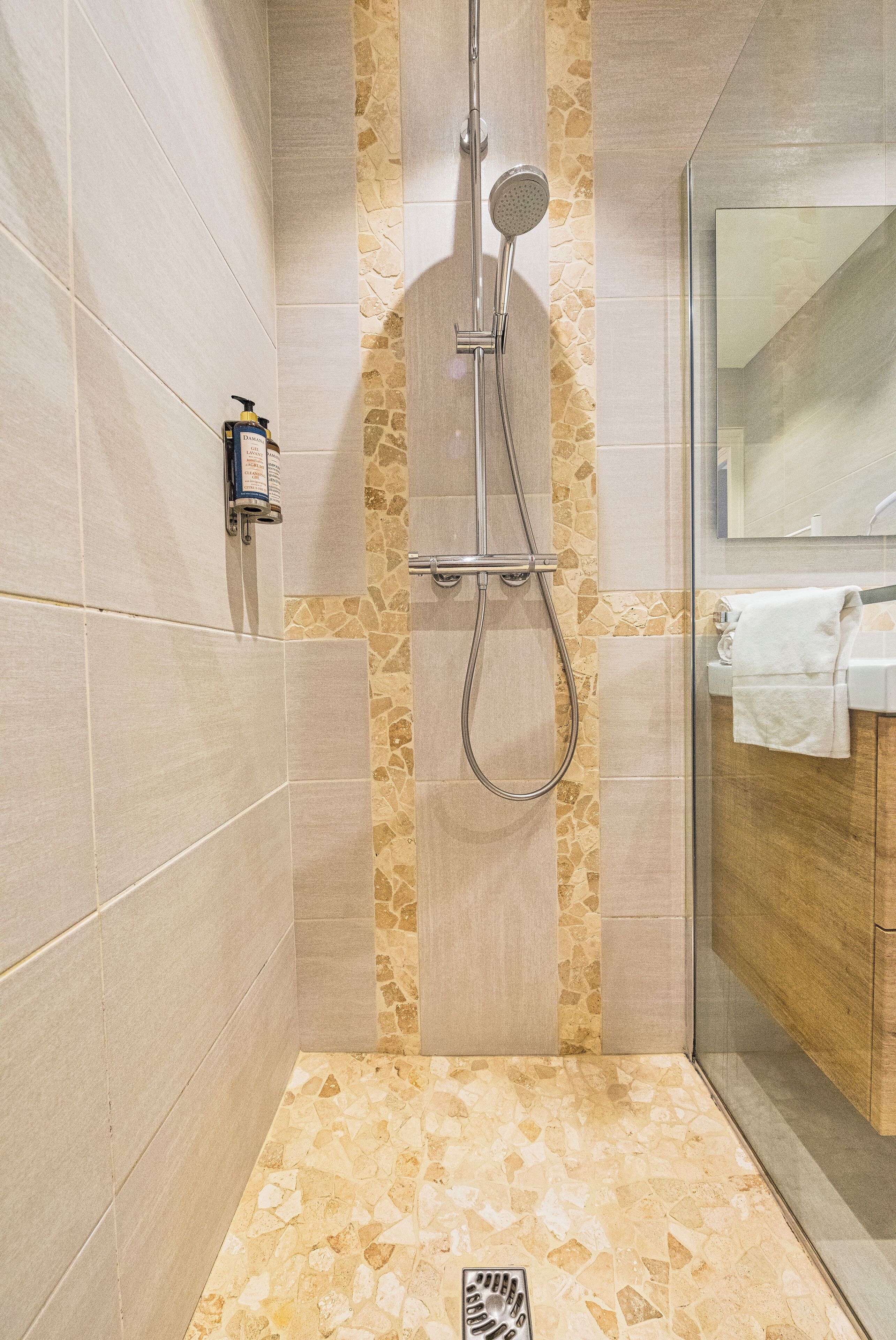 A modern shower with a handheld showerhead and a wall-mounted faucet, a glass shower enclosure, and a stone accent wall.