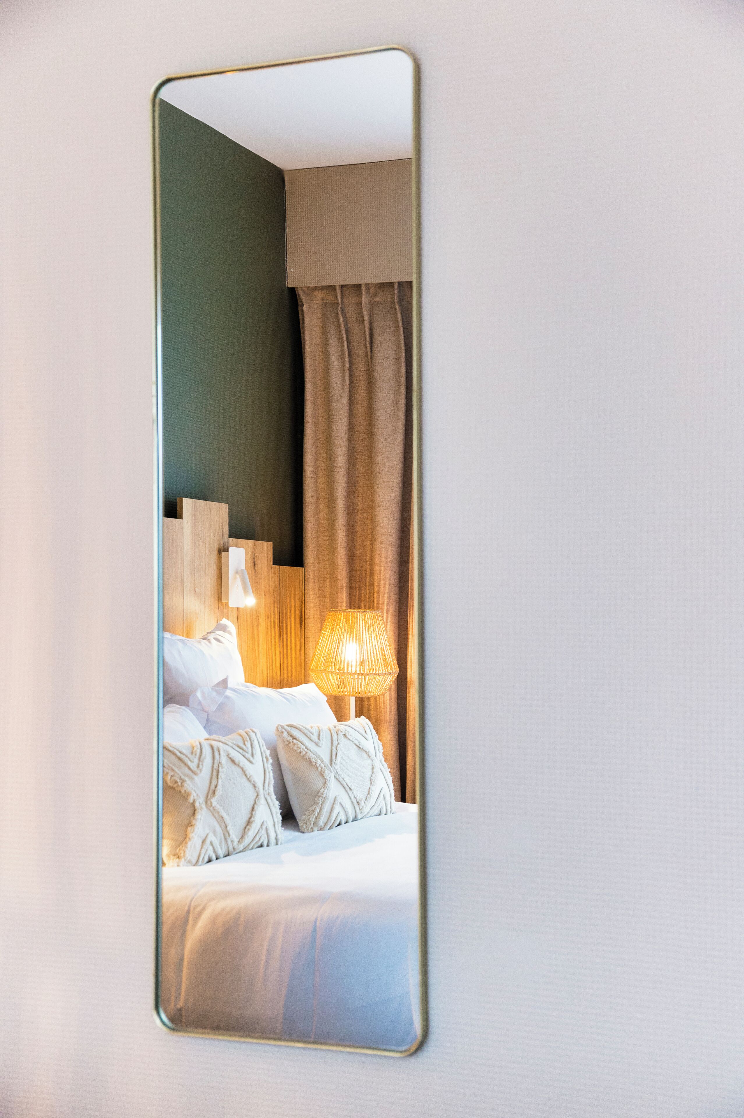 Quarto de hotel com cama, abajur e espelho na parede.