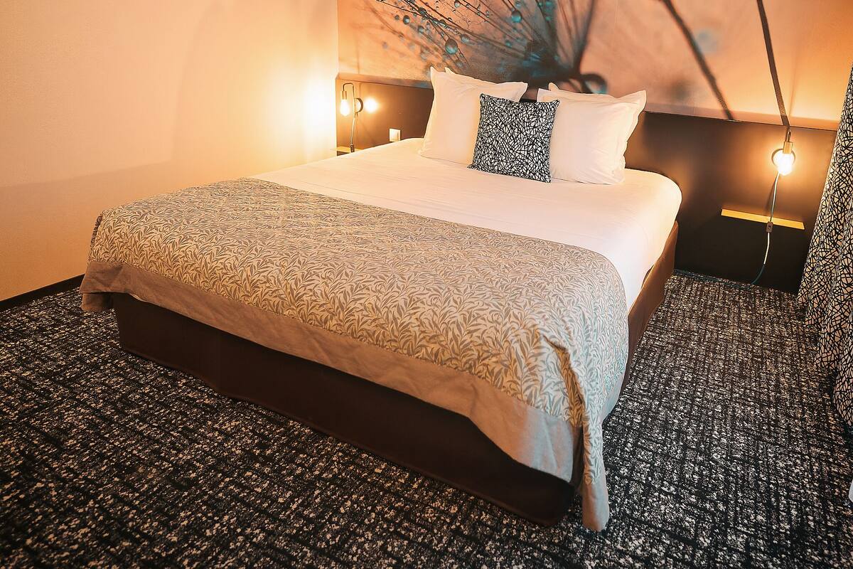 Une chambre d’hôtel avec un grand lit, une moquette à motifs, une œuvre d’art murale et des lampes de chevet.
