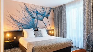 Habitación de hotel con una cama grande, una lámpara de pared y vistas al exterior a través de cortinas translúcidas.