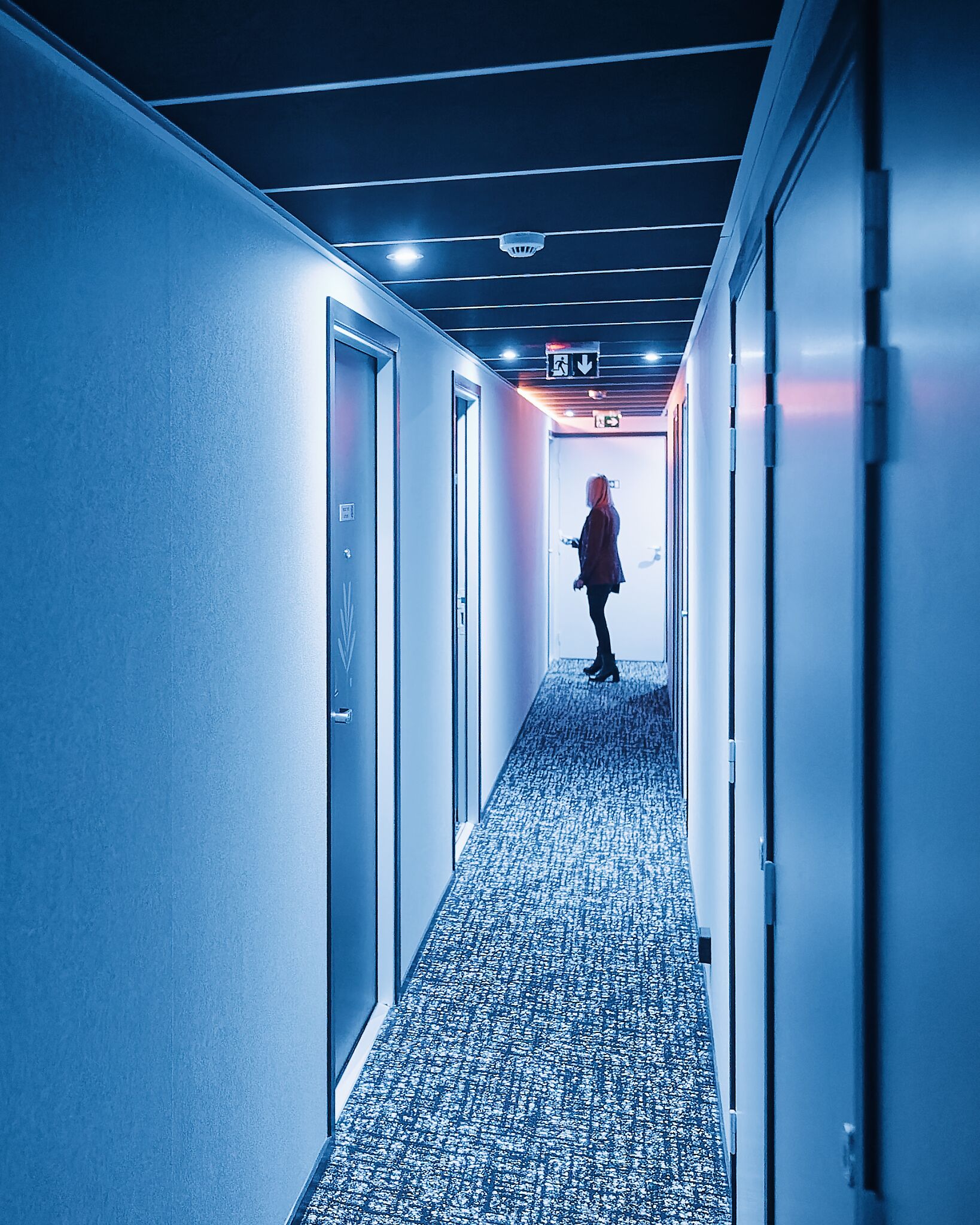 A hallway with a patterned carpet, doors on either side, and a person walking away from the camera.