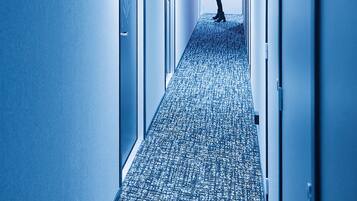 A hallway with a patterned carpet, doors on either side, and a person walking away from the camera.