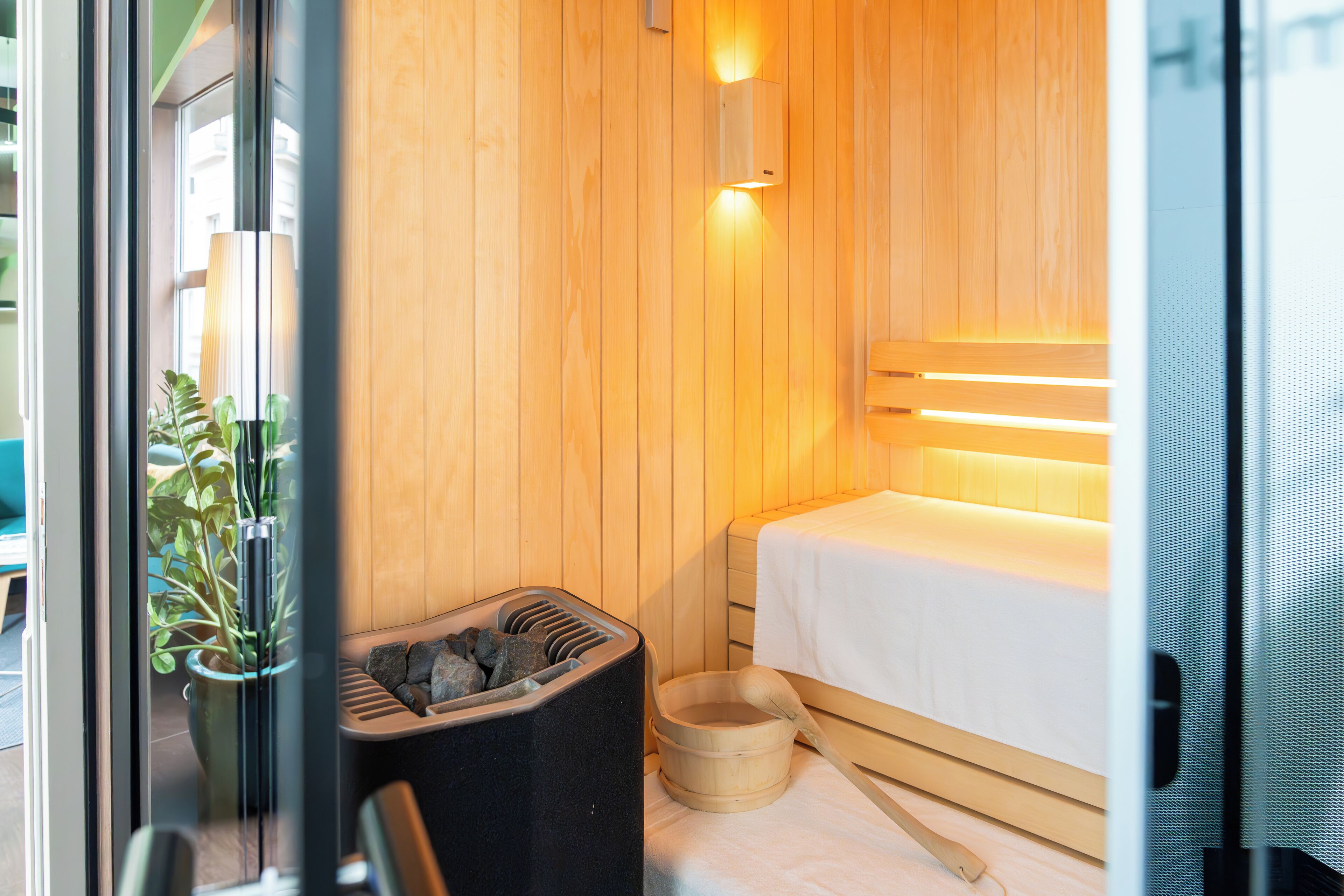 Una habitación pequeña y acogedora con paredes de madera, una cama, un cubo de madera y un bote de basura negro.