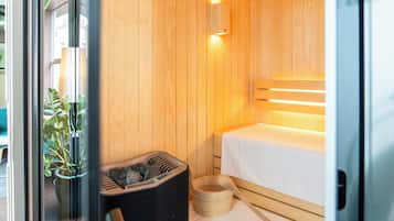 Una habitación pequeña y acogedora con paredes de madera, una cama, un cubo de madera y un bote de basura negro.