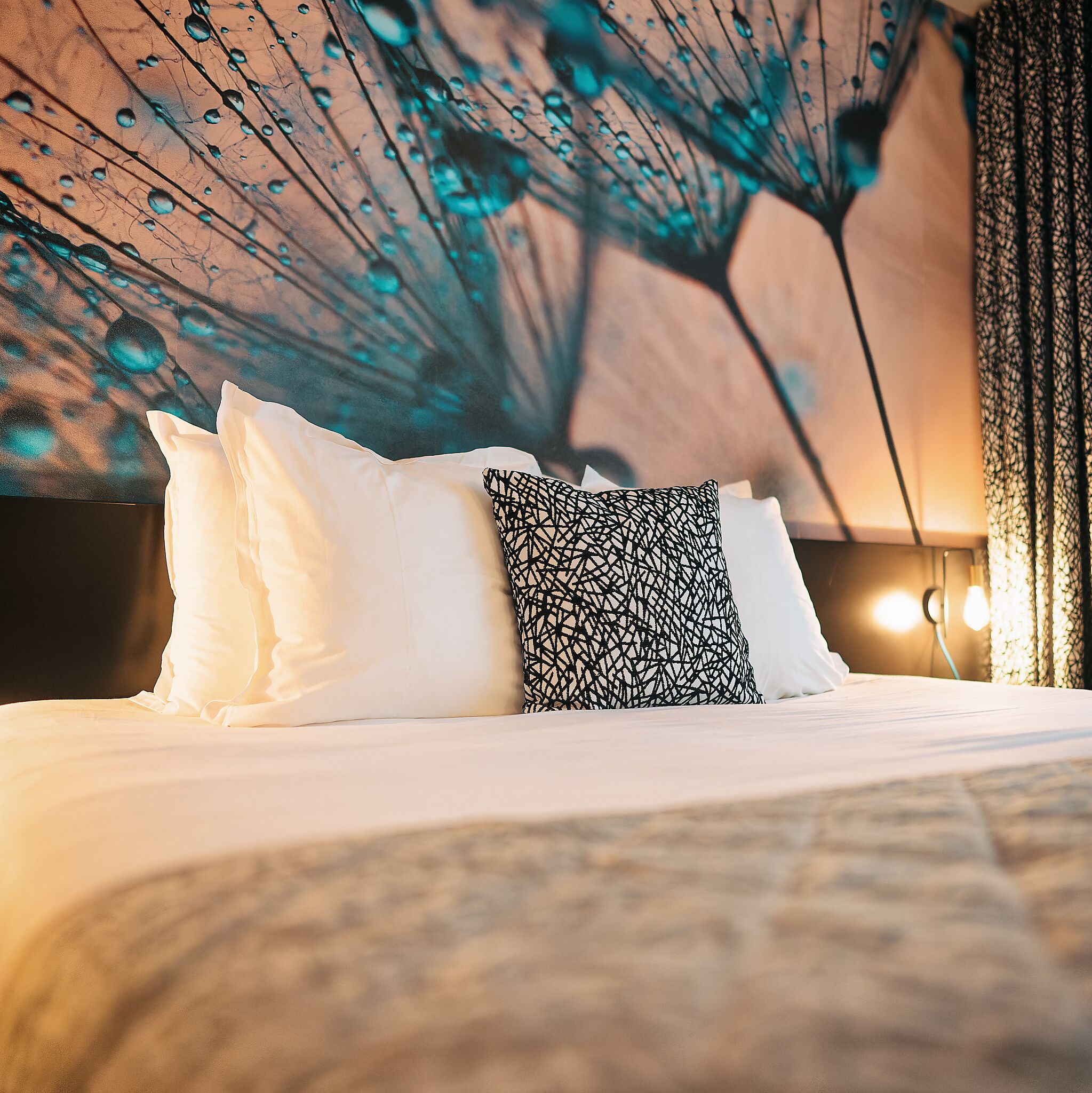 A bed with white and patterned pillows, a dark headboard, and a wall with a tree and raindrop design.
