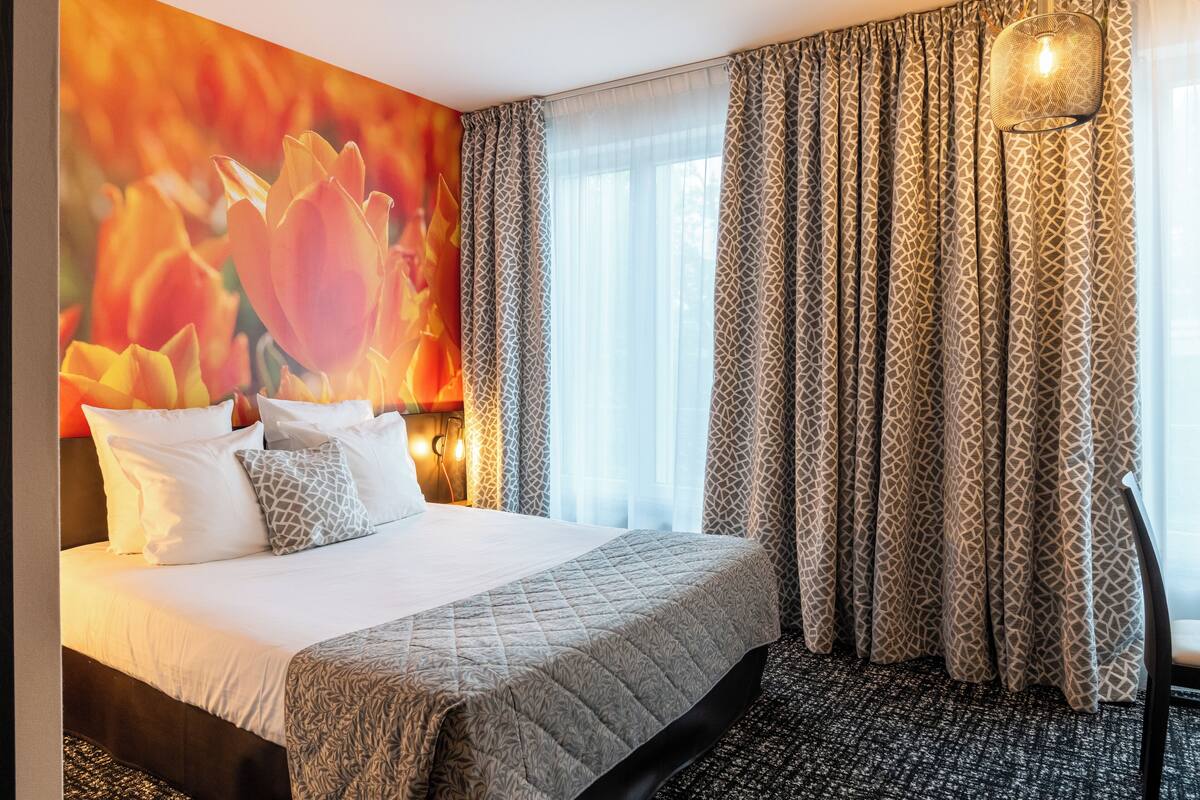 Une chambre d’hôtel avec un grand lit, une fresque murale à motifs et une fenêtre ornée de rideaux à motifs.