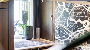 Un vestíbulo de hotel moderno con una planta grande en maceta, una alfombra estampada y una pared decorativa con un diseño geométrico.