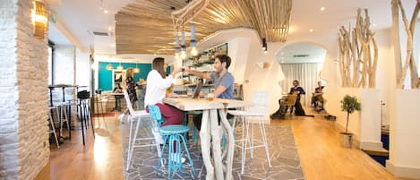 A modern interior with wooden flooring, a central table with chairs, and a bar area in the background.