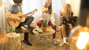A cozy indoor setting with a guitar player, a woman holding a drink, and a cactus plant on a small table. - La Finca Hôtel  (Paris)
